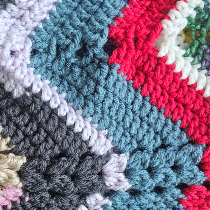 Colorful crocheted blanket with a geometric pattern on a light purple background