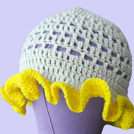 Crocheted white hat with yellow trim on a mannequin head against a purple background